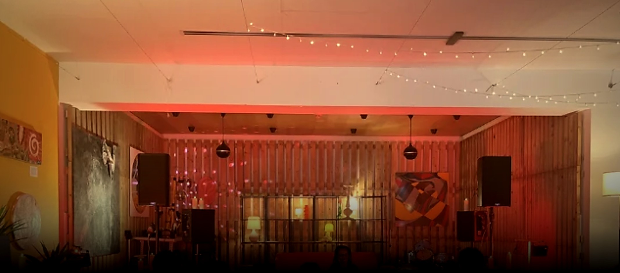 The performance space, red lit wooden wall, string lights and a low stage